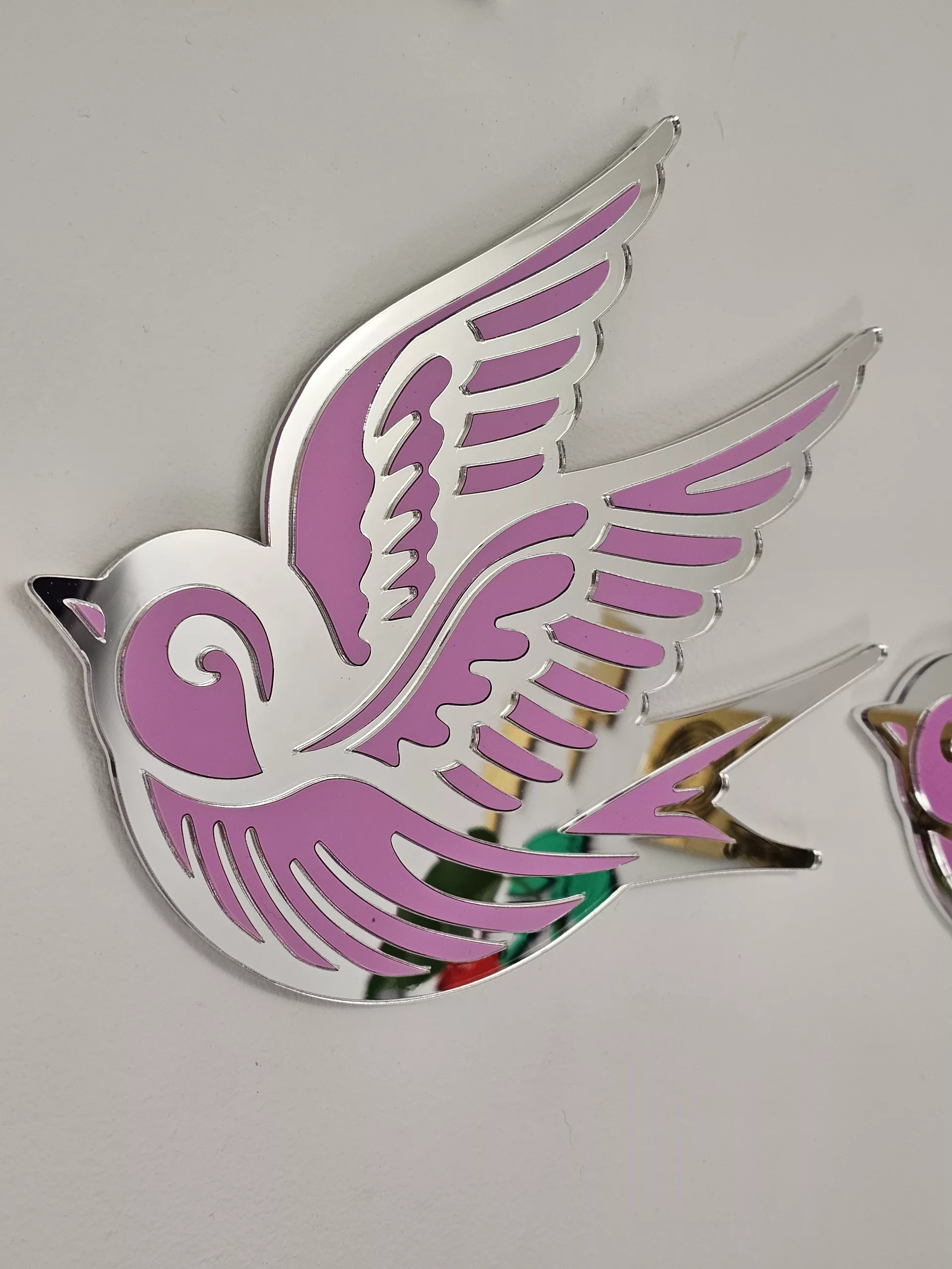 A piece of wall art in the shape of a swallow, made from pink and silver mirror acrylic.
