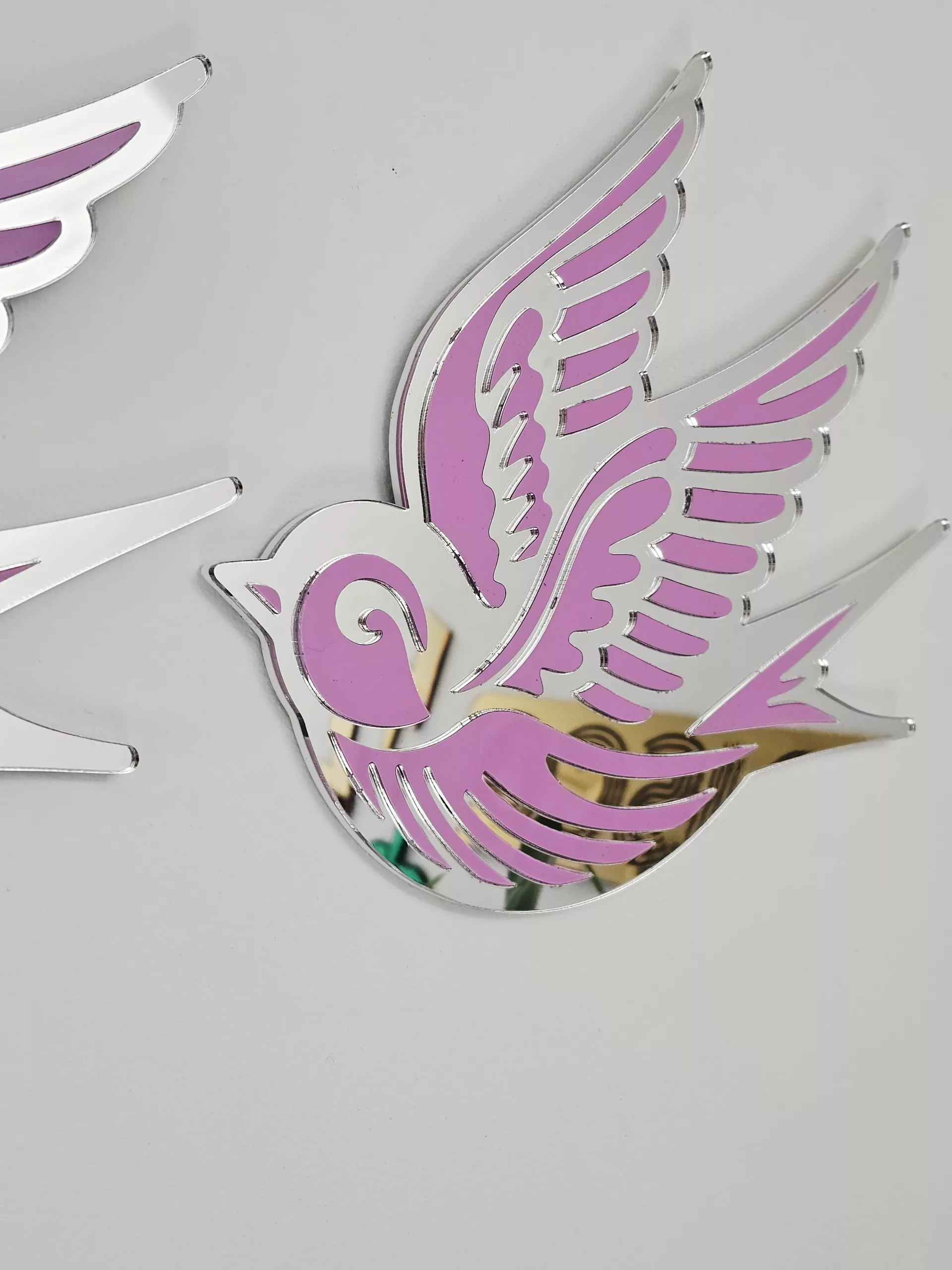 A piece of wall art in the shape of a swallow, made from pink and silver mirror acrylic.