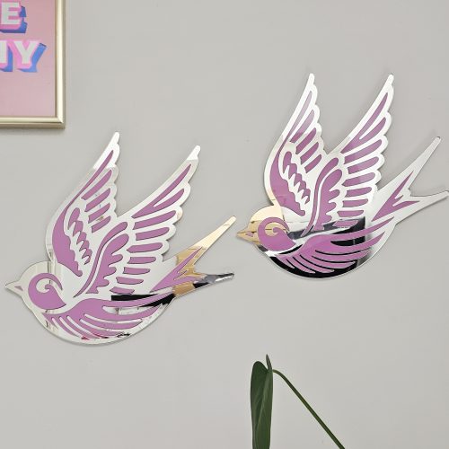 A piece of wall art in the shape of a swallow, made from pink and silver mirror acrylic.