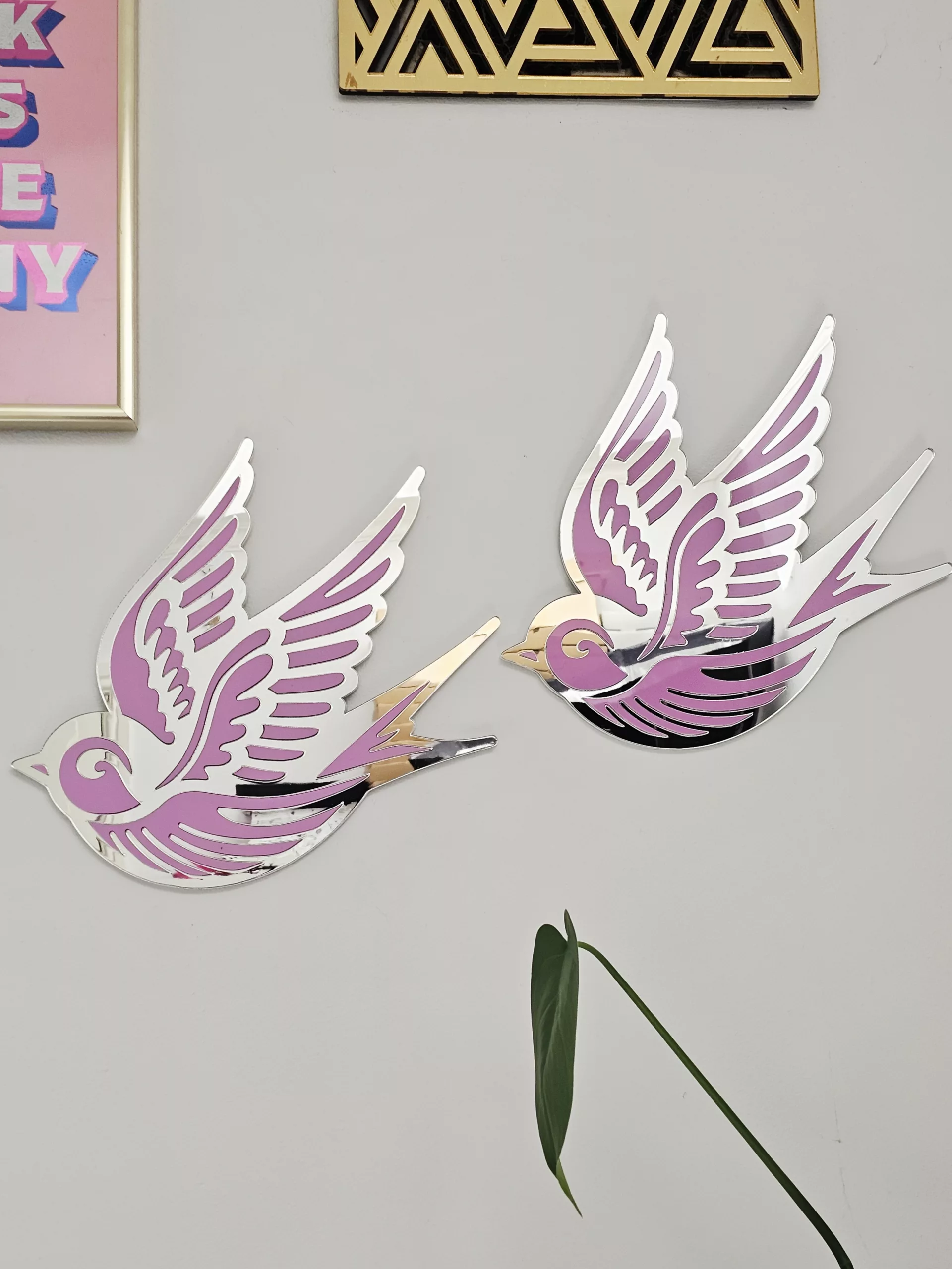A piece of wall art in the shape of a swallow, made from pink and silver mirror acrylic.