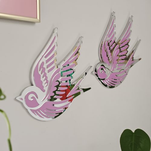 A piece of wall art in the shape of a swallow, made from pink and silver mirror acrylic.