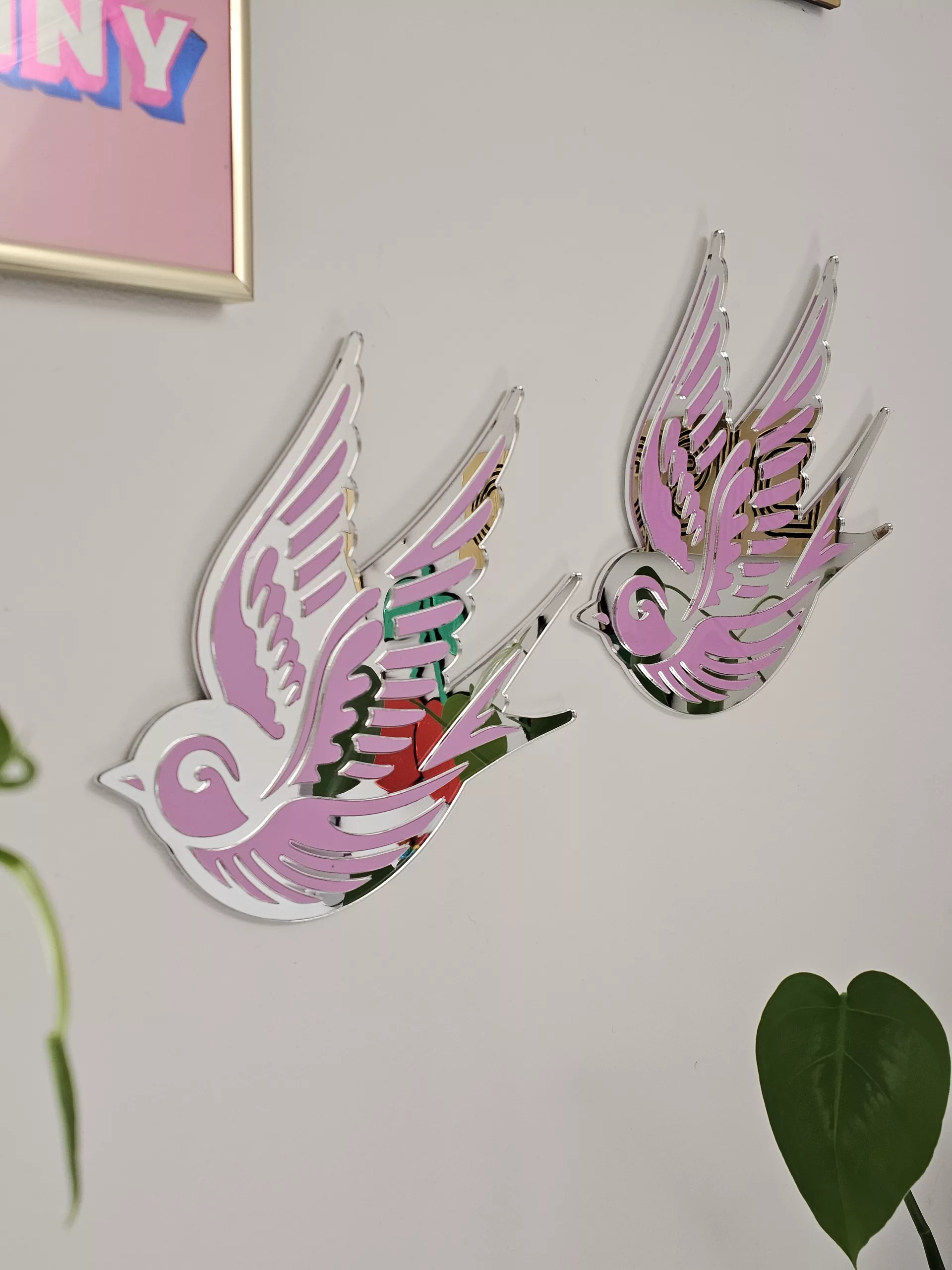 A piece of wall art in the shape of a swallow, made from pink and silver mirror acrylic.