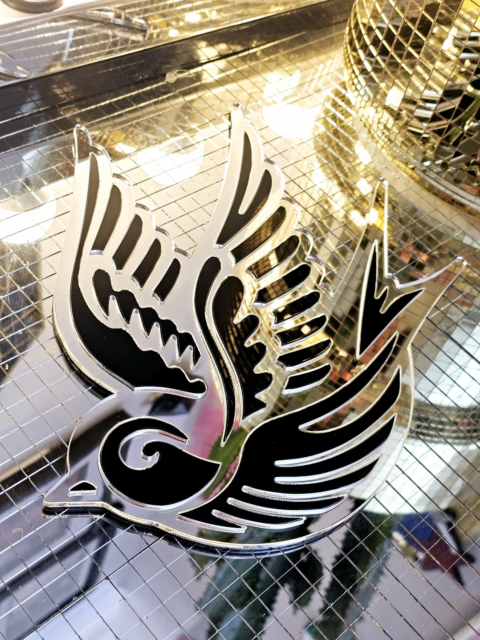 A piece of handmade wall art in the shape of a swallow with a silver mirror outline and black gloss details.