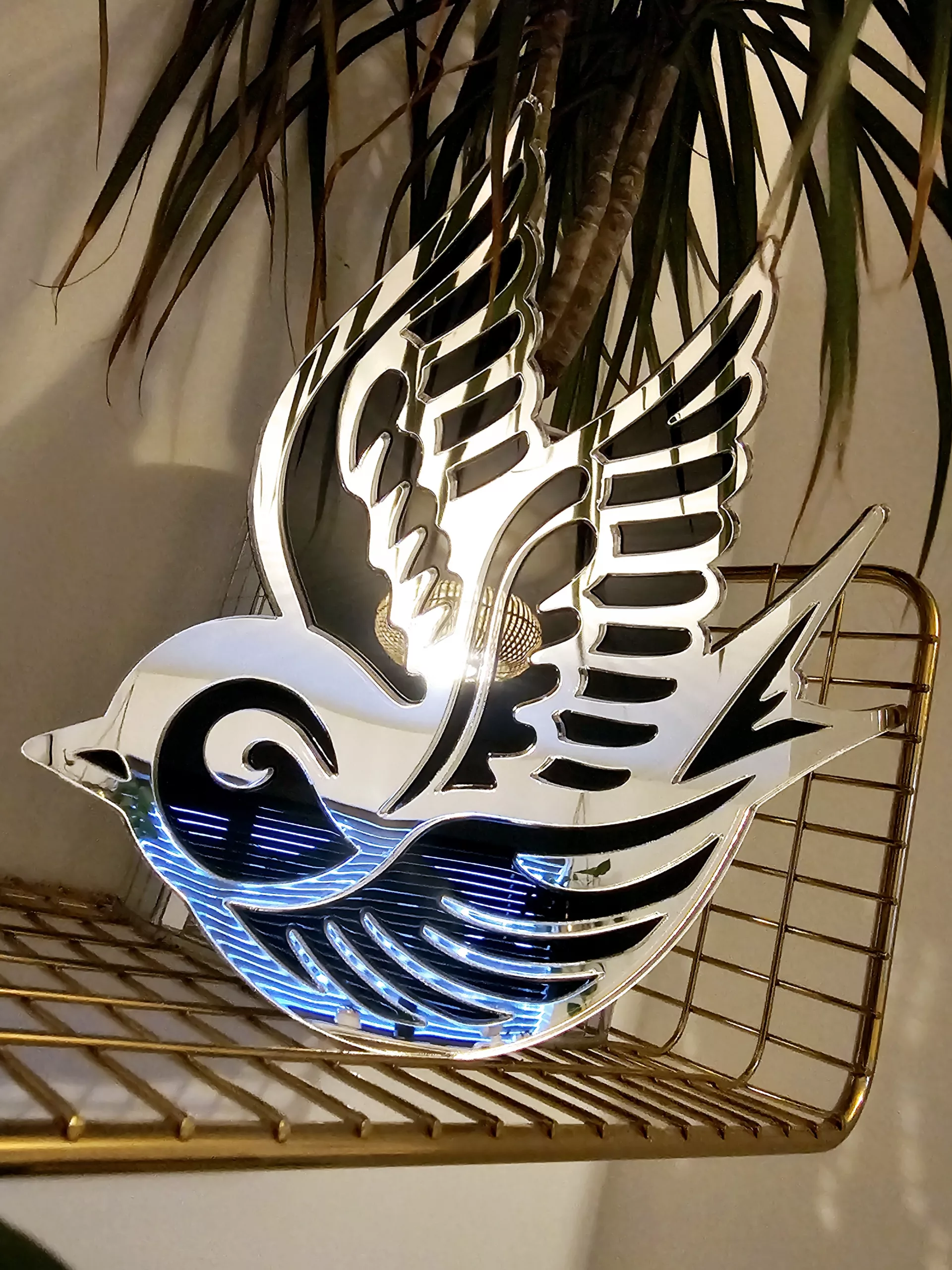 A piece of handmade wall art in the shape of a swallow with a silver mirror outline and black gloss details.