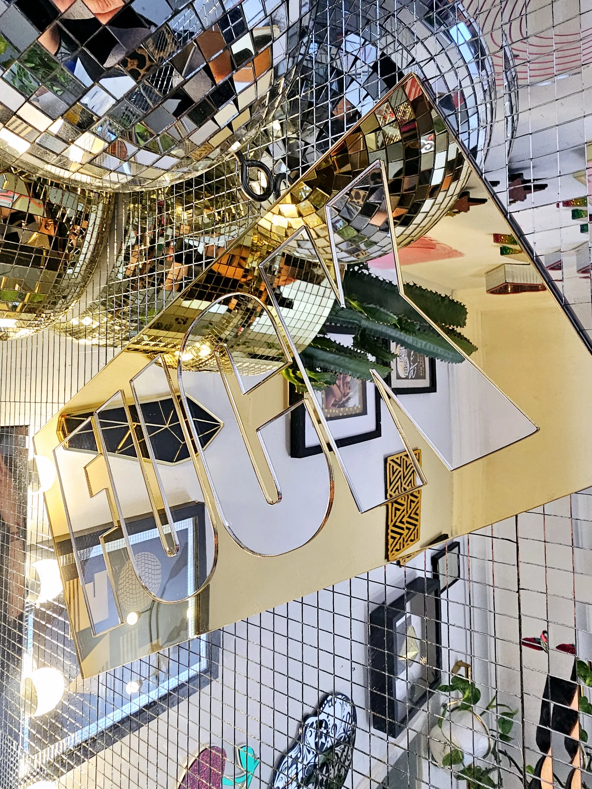 A mirror with the word FUCK in silver lettering with a gold mirror outline.