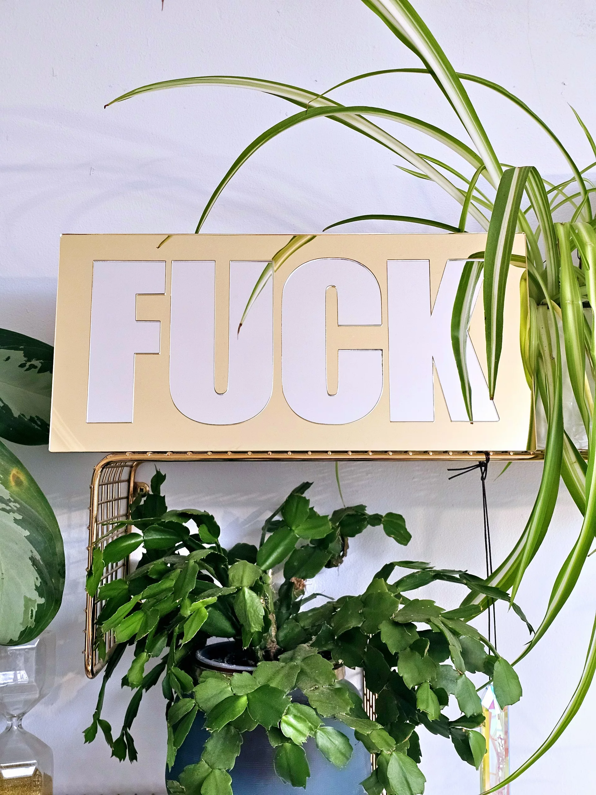 A mirror with the word FUCK in silver lettering with a gold mirror outline.