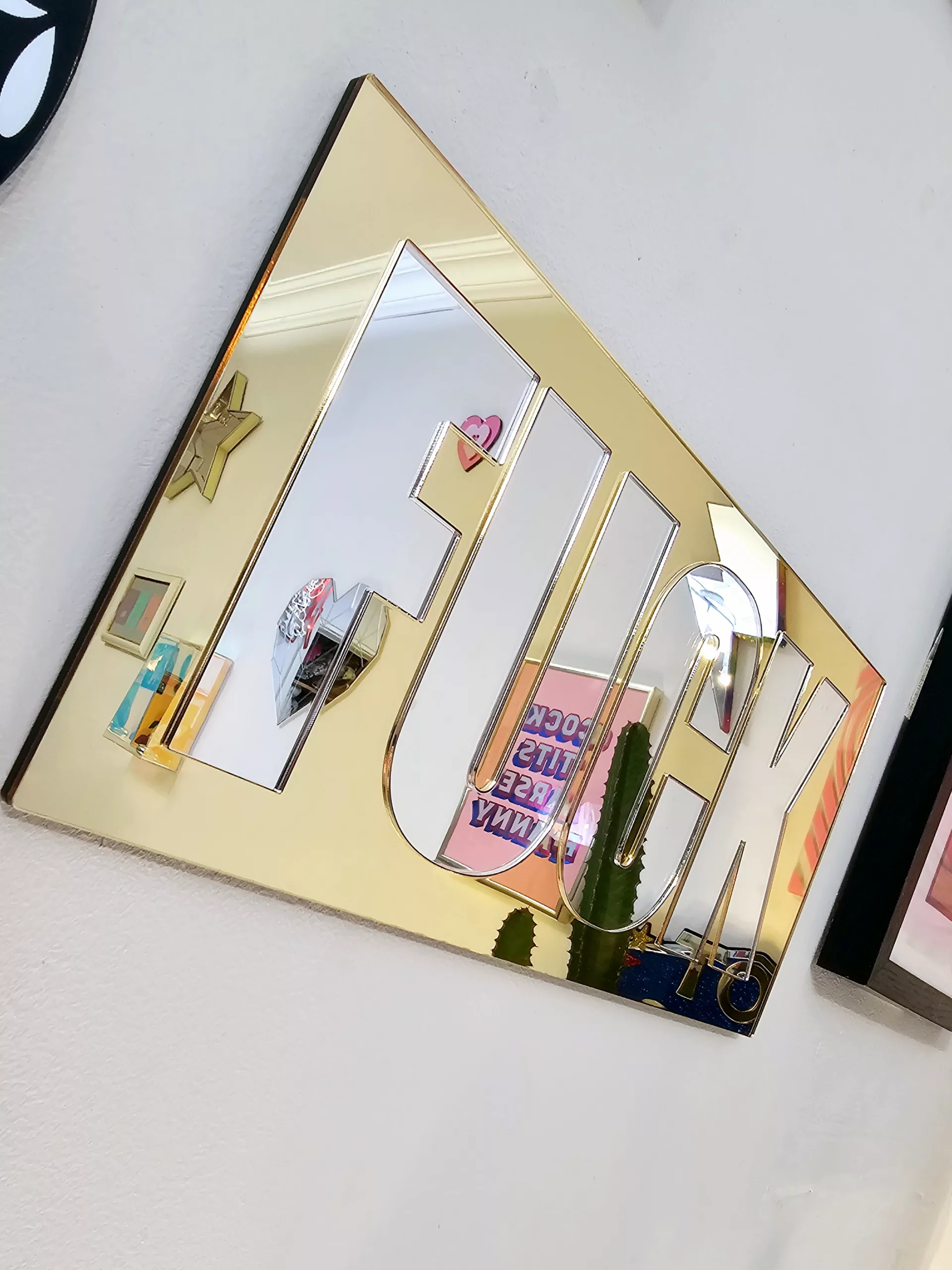 A mirror with the word FUCK in silver lettering with a gold mirror outline.