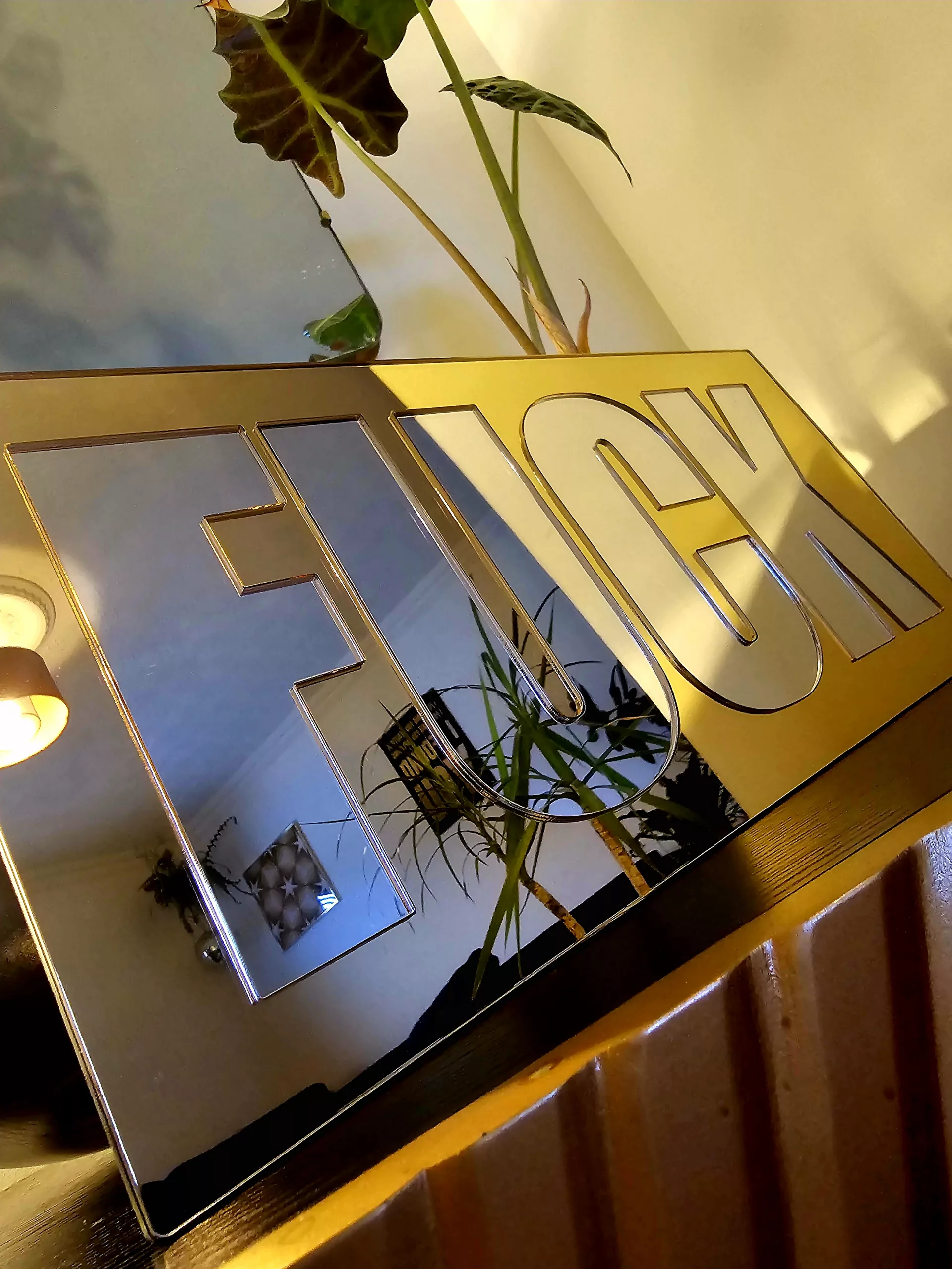 A mirror with the word FUCK in silver lettering with a gold mirror outline.