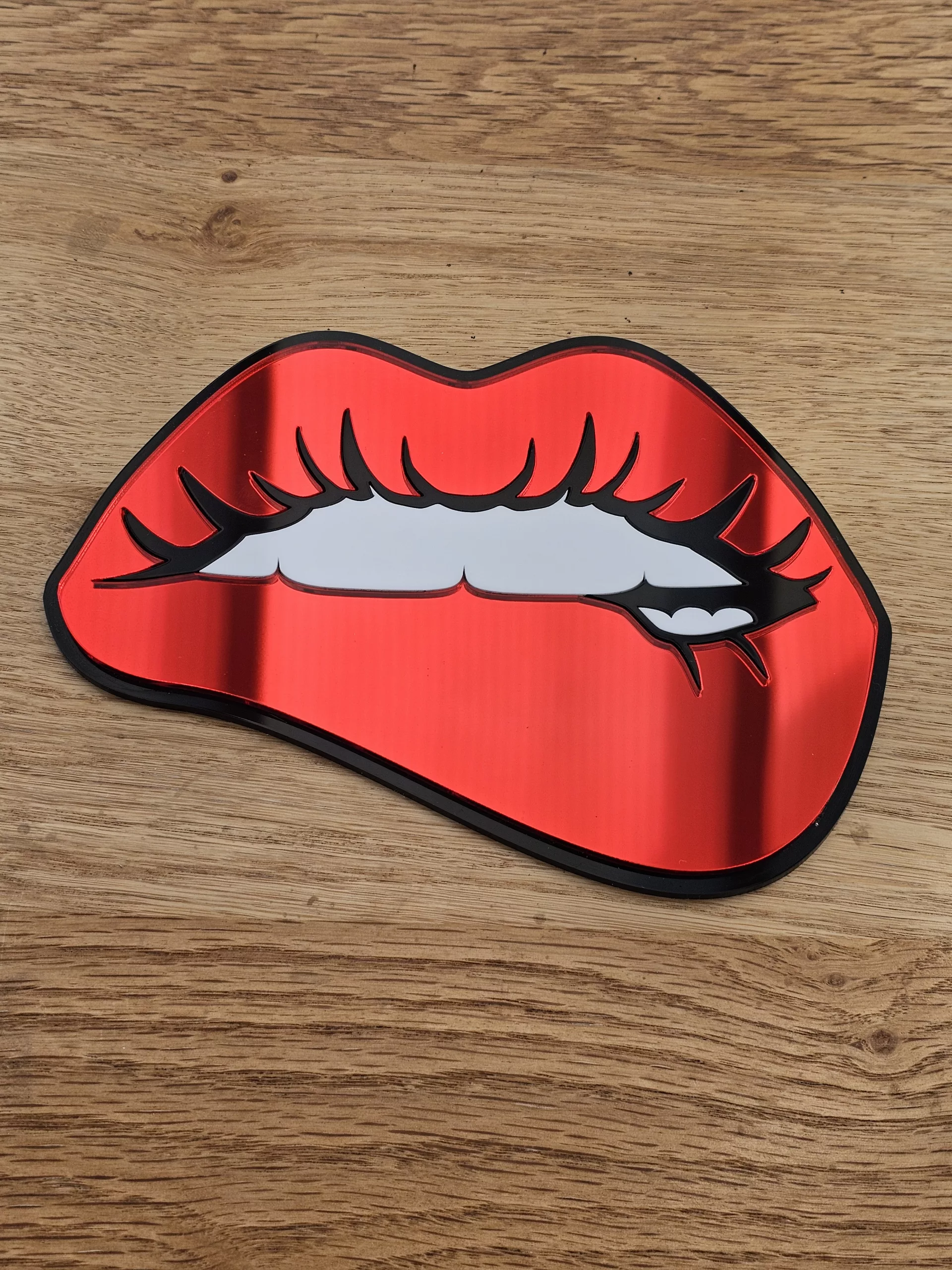 A handmade mirror in the shape of lips with the bottom lip being bitten. Made with mirror lips and glossy white teeth.