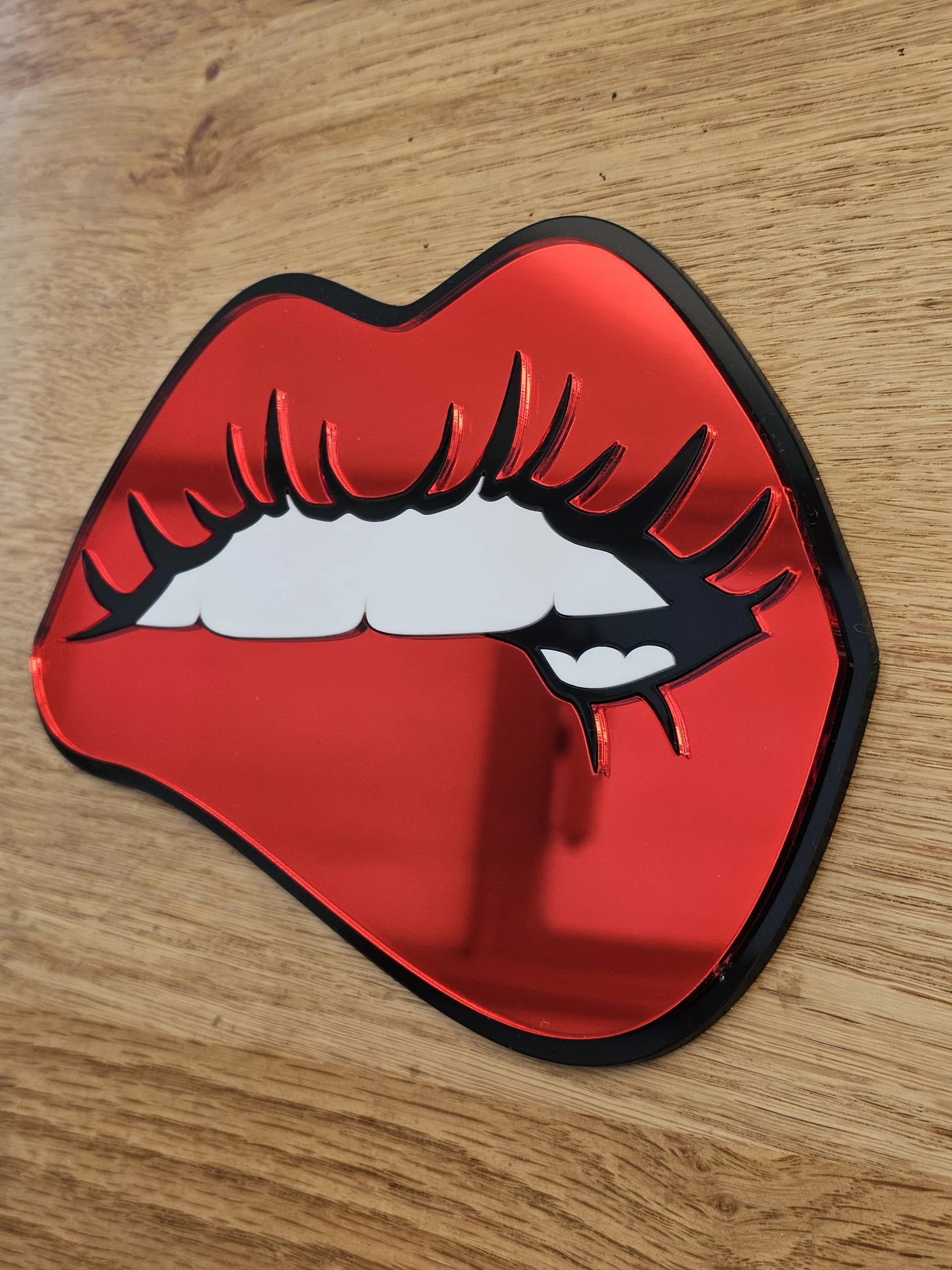 A handmade mirror in the shape of lips with the bottom lip being bitten. Made with mirror lips and glossy white teeth.