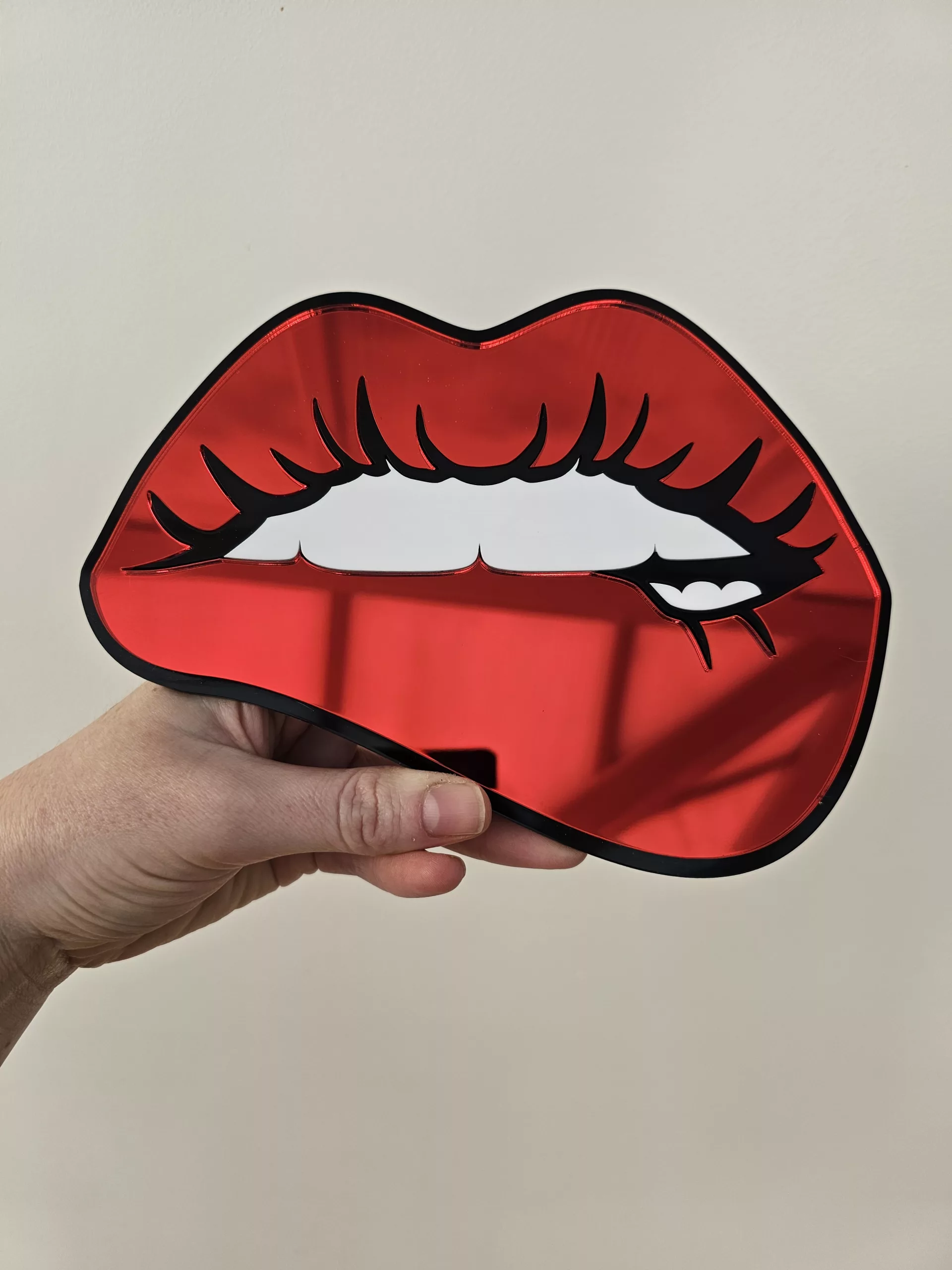 A handmade mirror in the shape of lips with the bottom lip being bitten. Made with mirror lips and glossy white teeth.