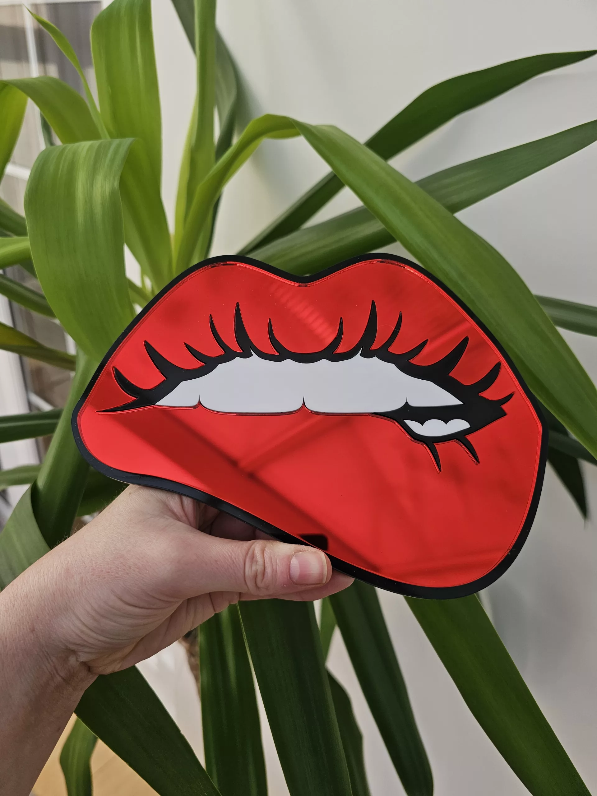A handmade mirror in the shape of lips with the bottom lip being bitten. Made with mirror lips and glossy white teeth.