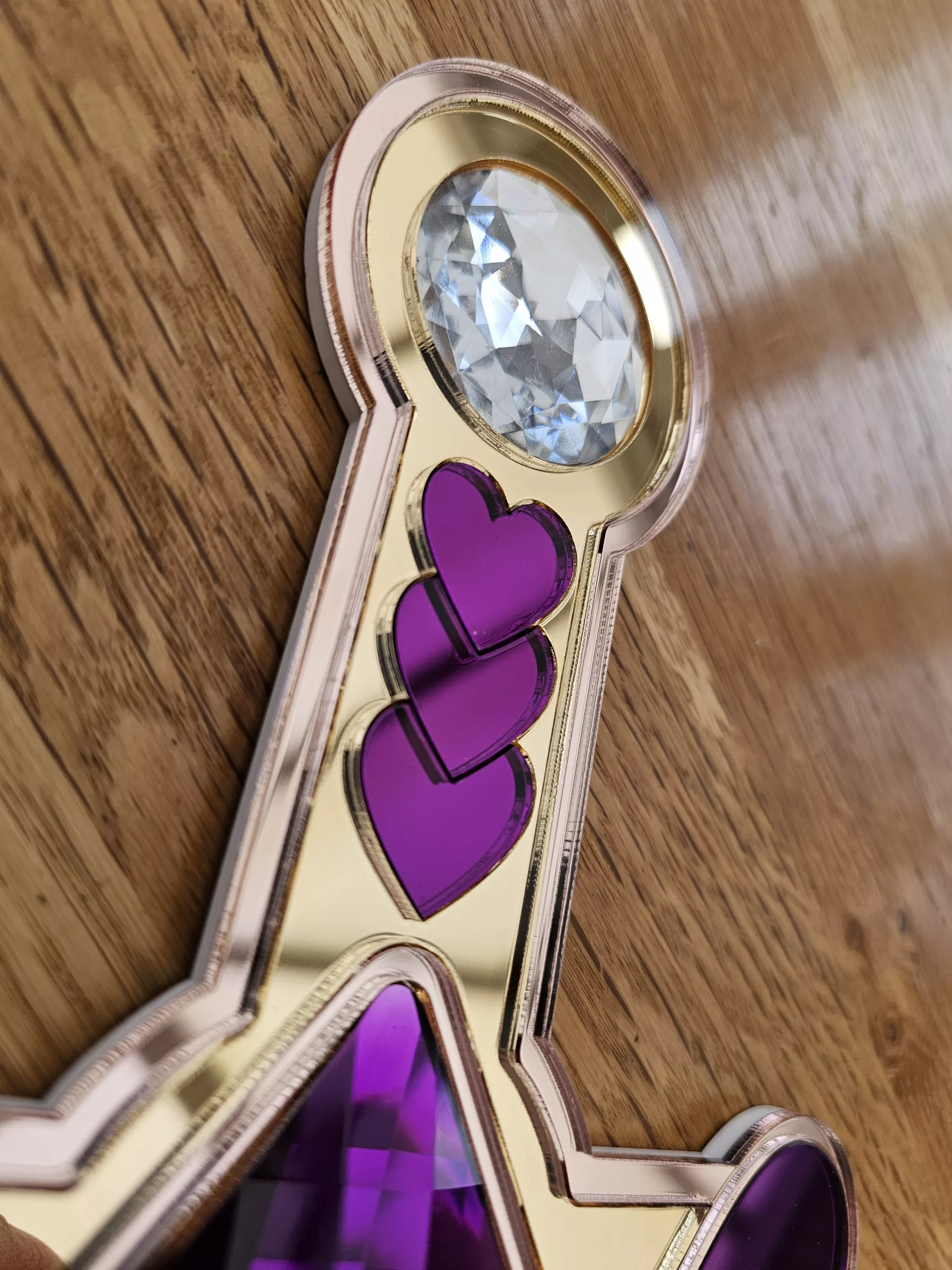 A handmade piece of wall art in the shape of a heart and sword. Made with purple mirror, gem and glitter accents.