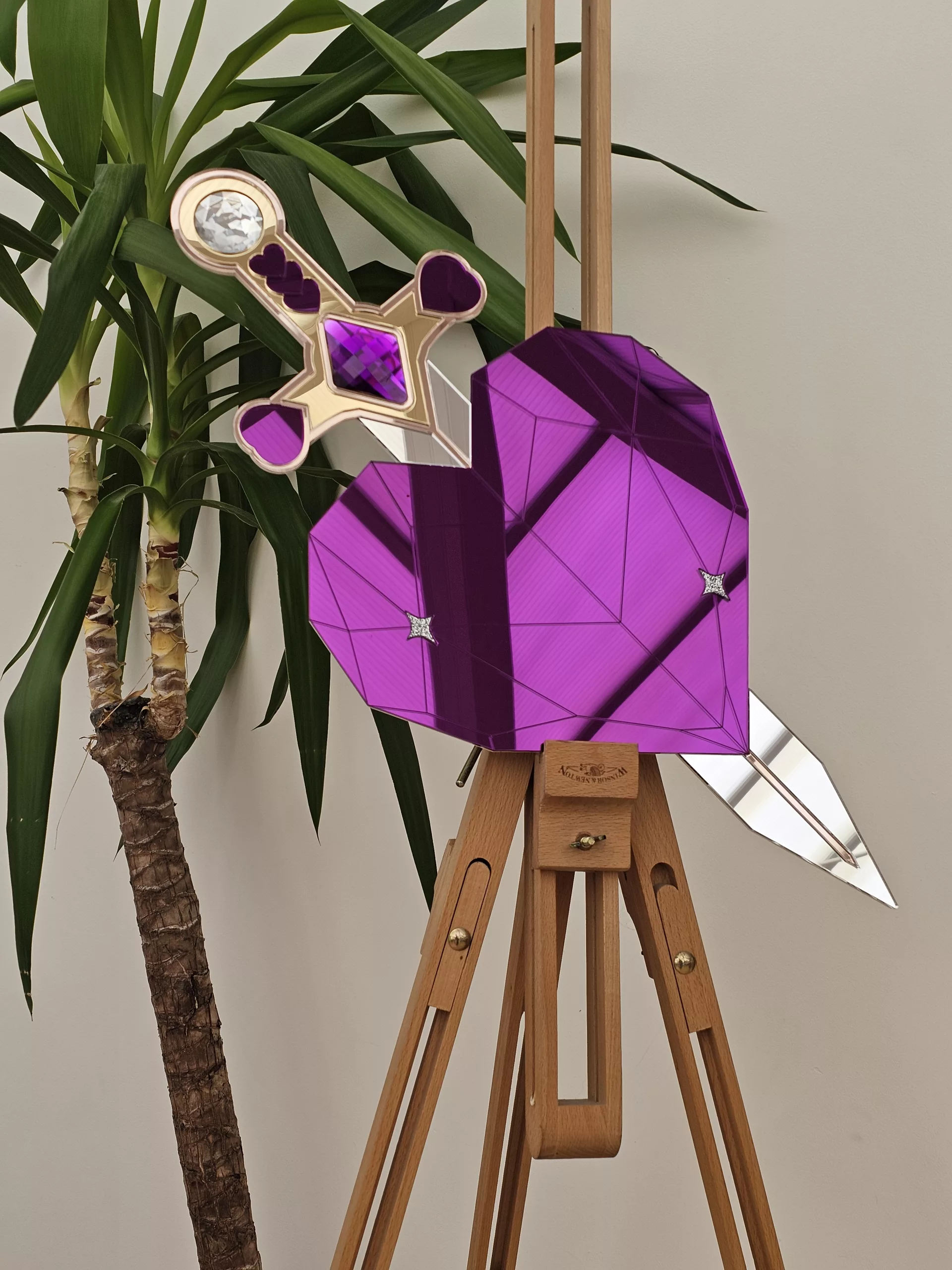A handmade piece of wall art in the shape of a heart and sword. Made with purple mirror, gem and glitter accents.