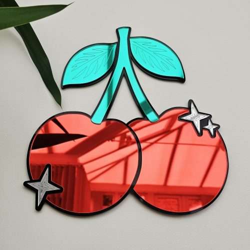 A piece of mirrored wall art in the shape of a cherry. With green leaves and silver sparkle details.