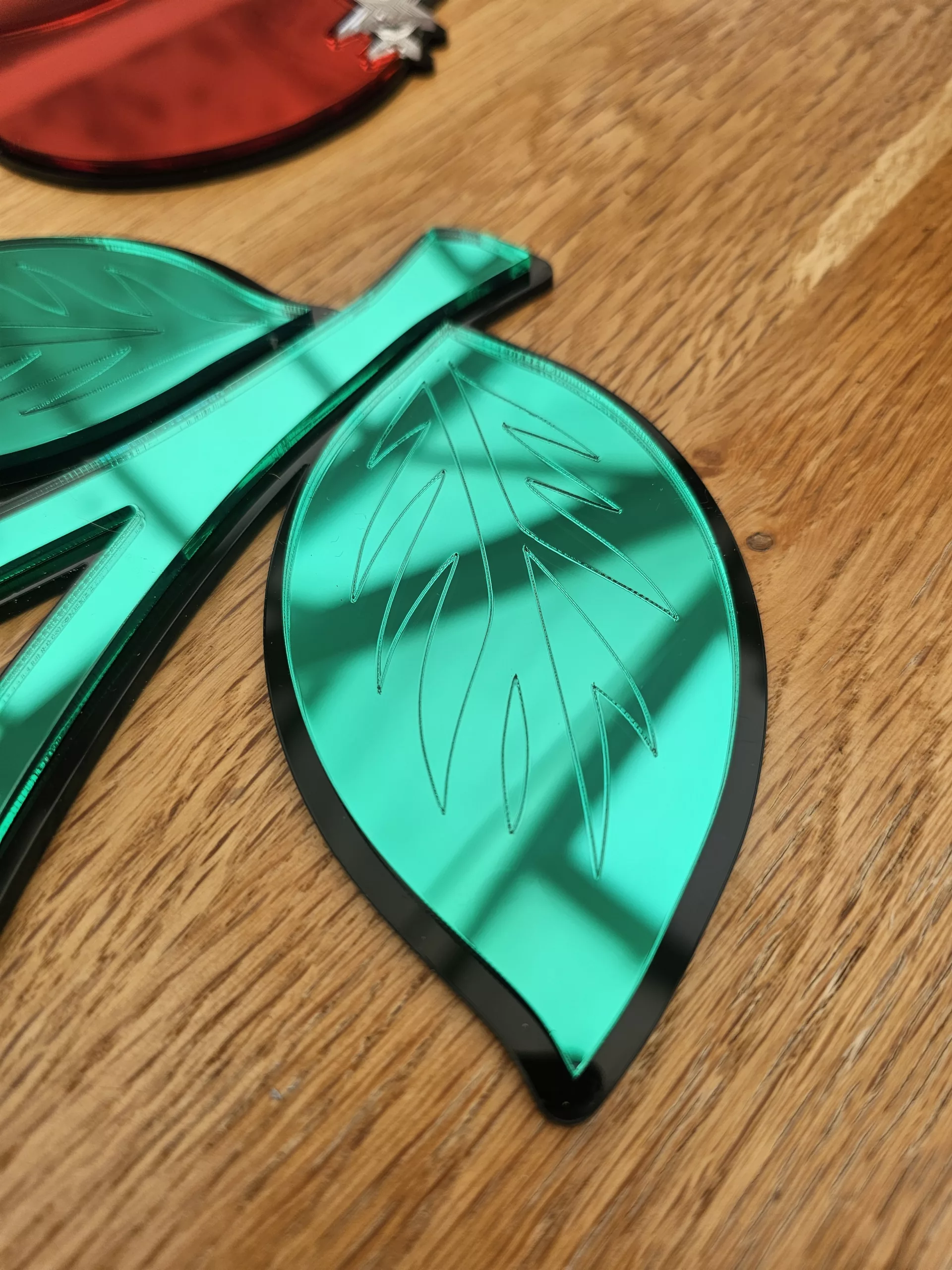A piece of mirrored wall art in the shape of a cherry. With green leaves and silver sparkle details.