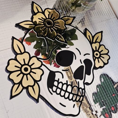 A mirror in the shape of a skull and flowers in an old school tattoo style.