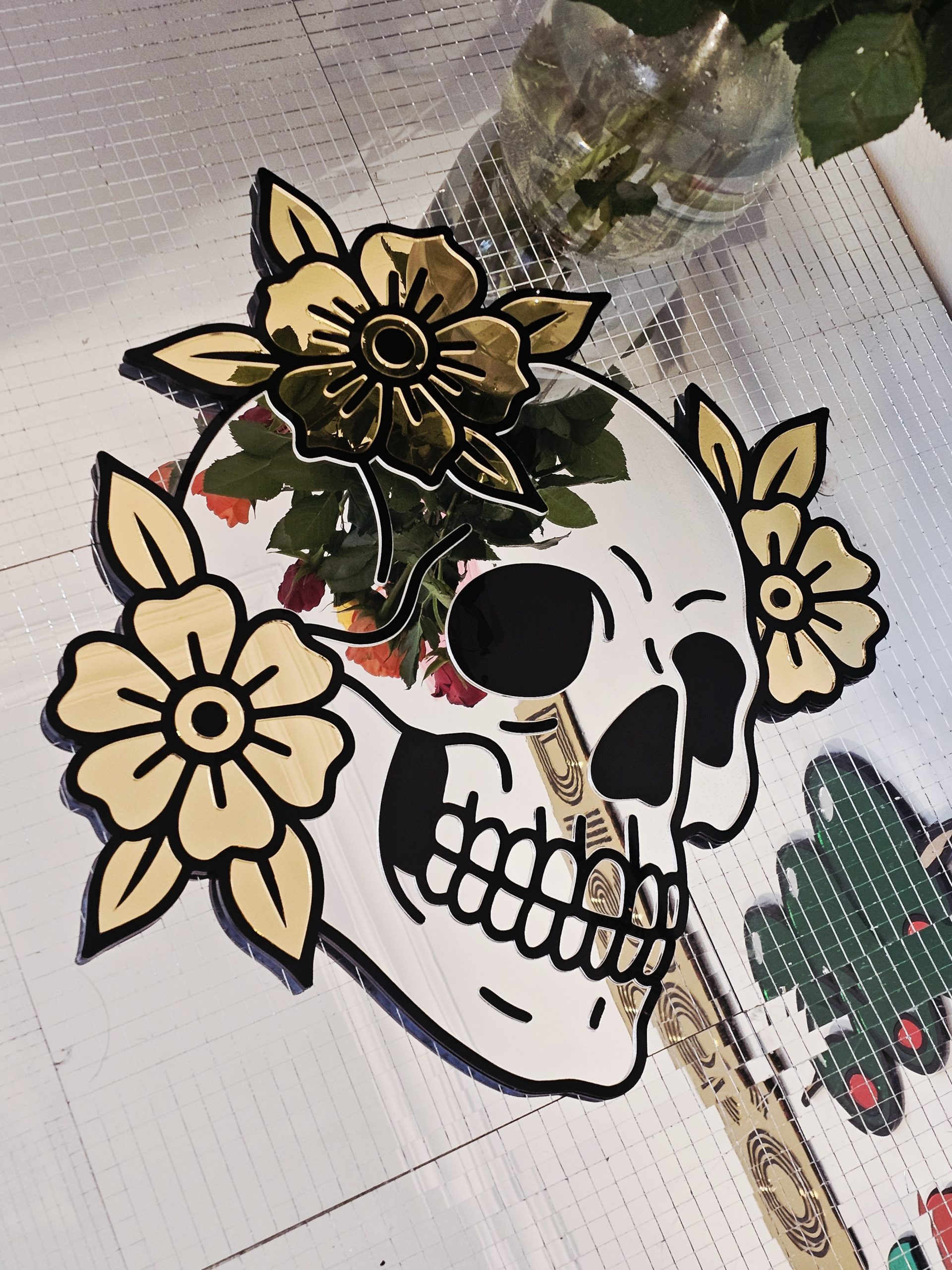 A mirror in the shape of a skull and flowers in an old school tattoo style.