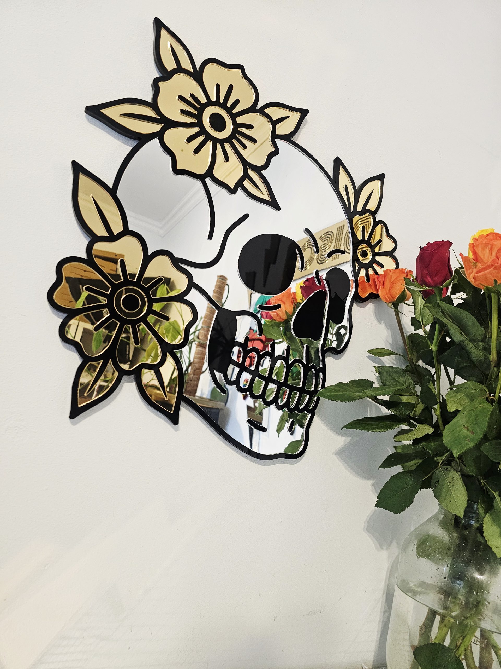 A mirror in the shape of a skull and flowers in an old school tattoo style.