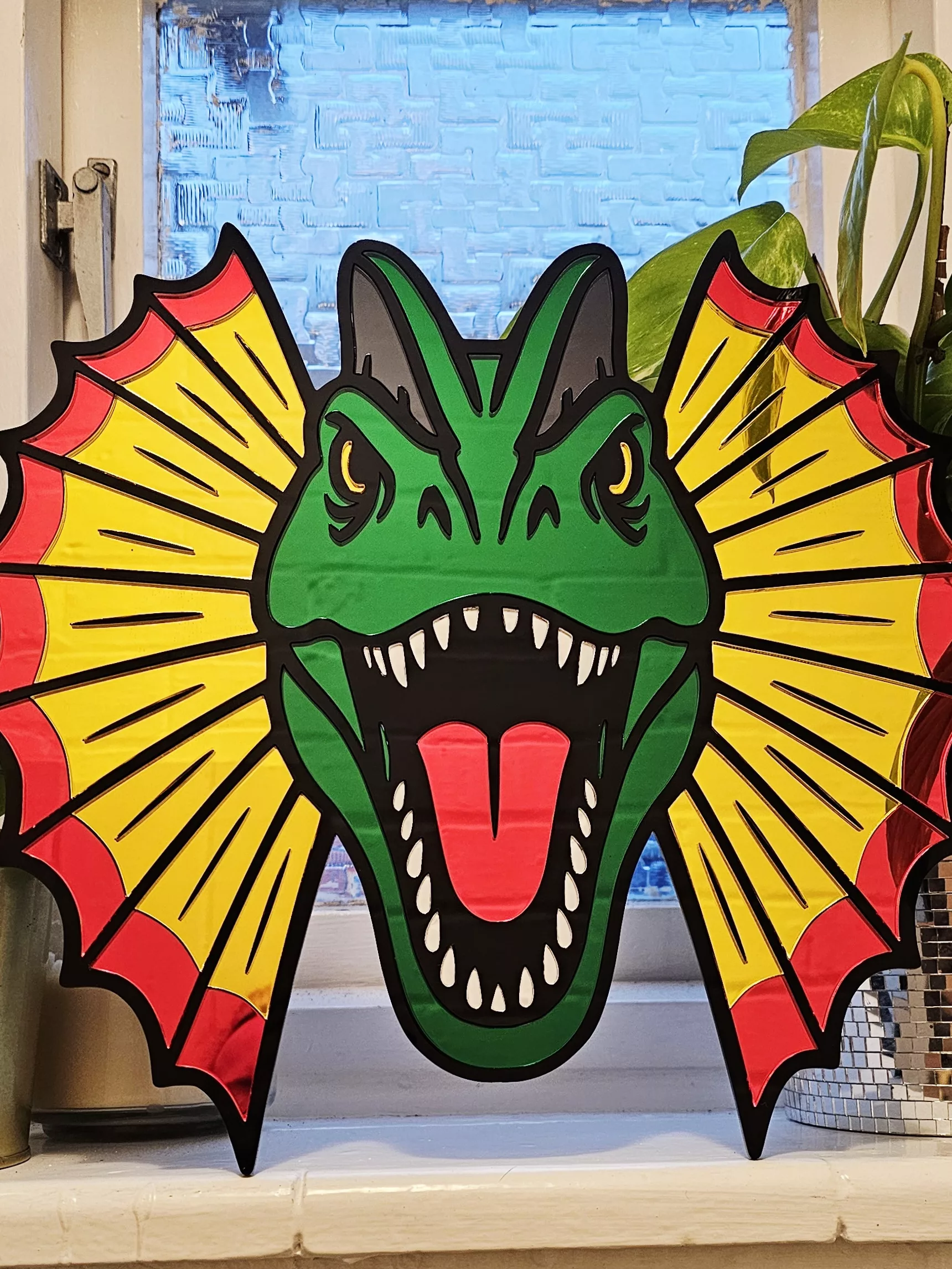 Colourful mirrored acrylic wall art in the shape of a Dilophosaurus dinosaur.