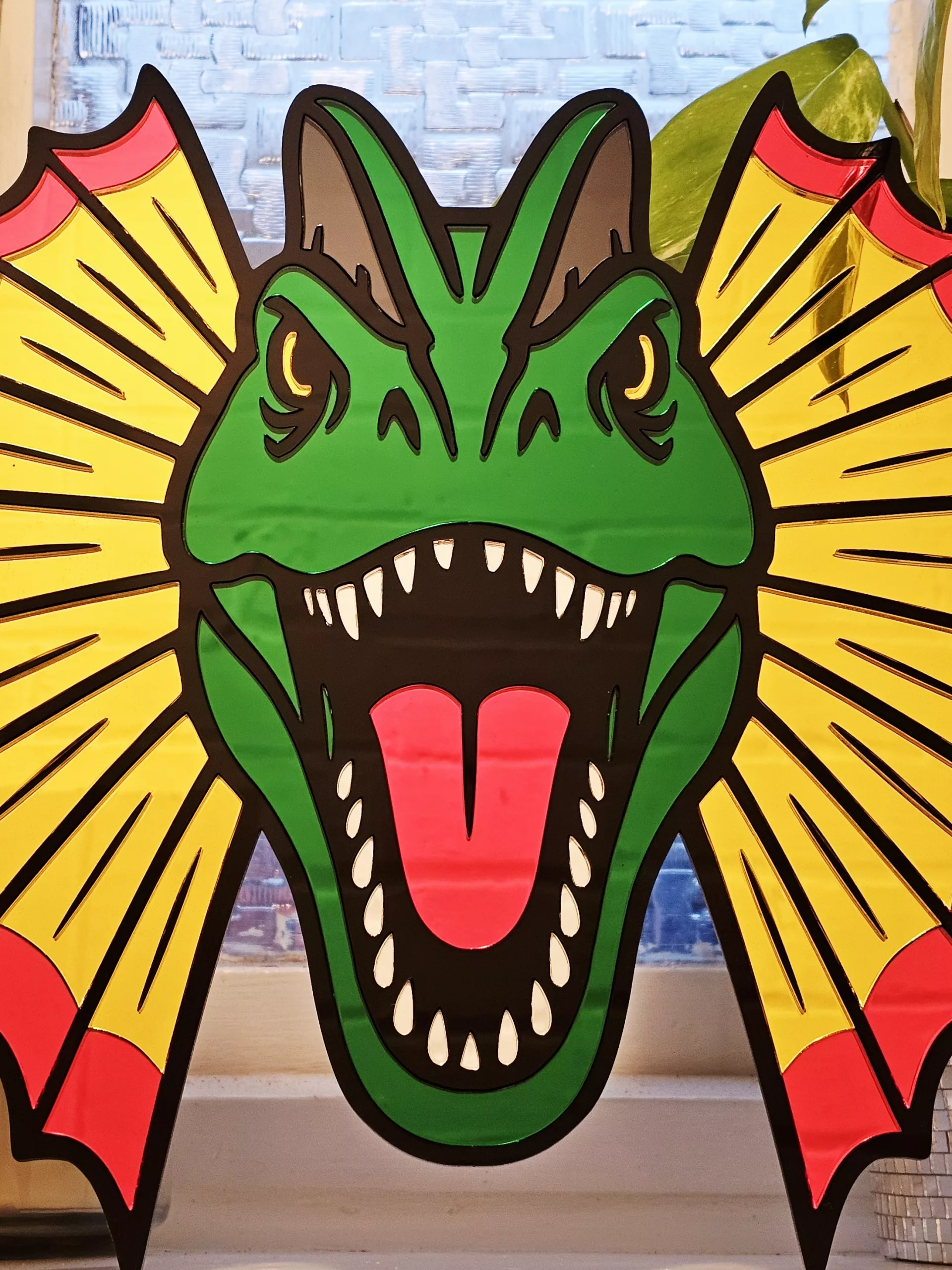 Colourful mirrored acrylic wall art in the shape of a Dilophosaurus dinosaur.