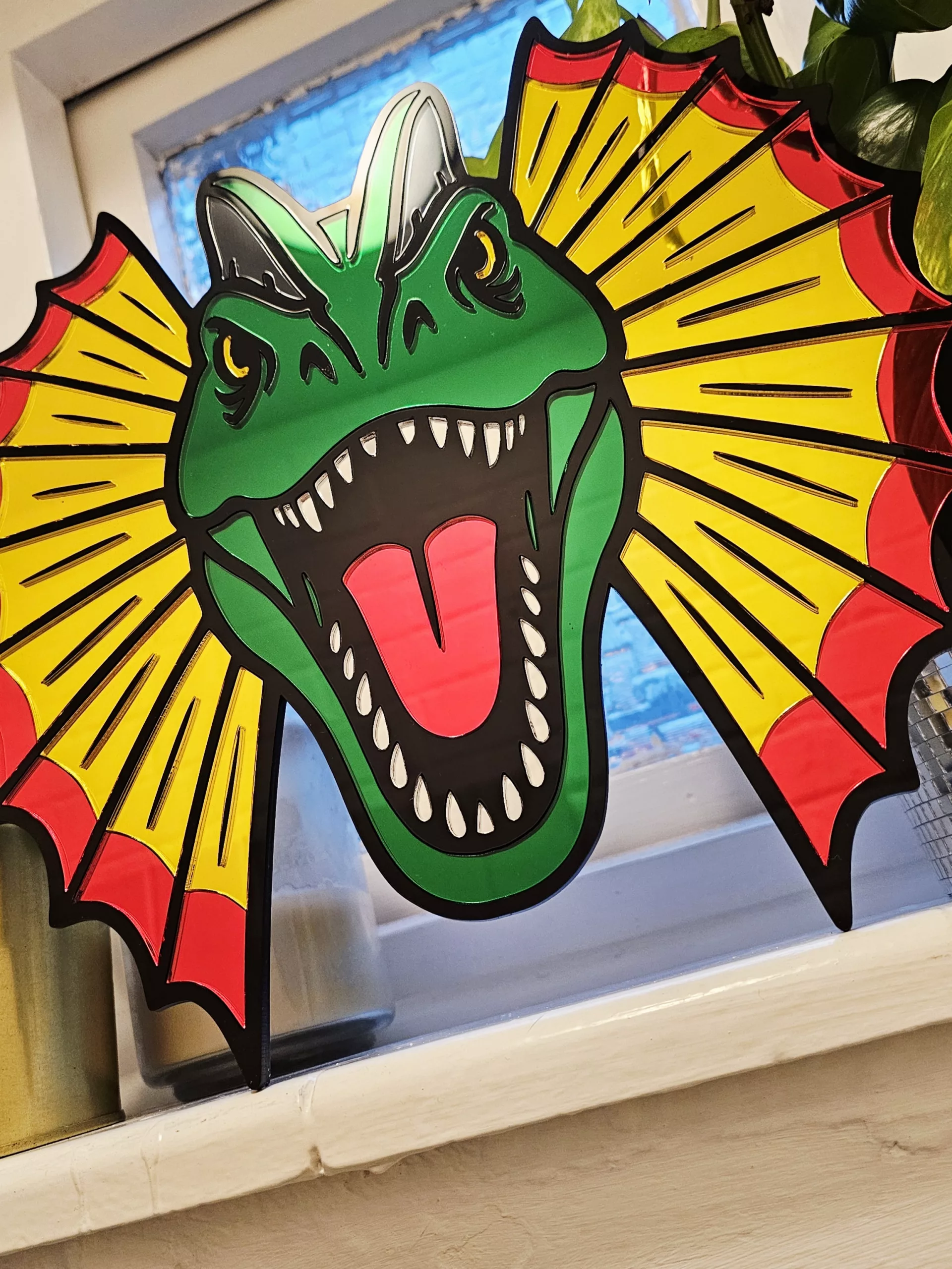 Colourful mirrored acrylic wall art in the shape of a Dilophosaurus dinosaur.