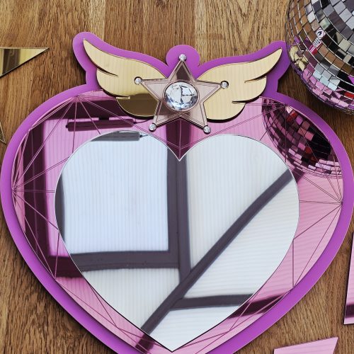 A heart mirror. Woth pink frame, layered with pink and silver heart, with details including gold wings inlaid with crystals.