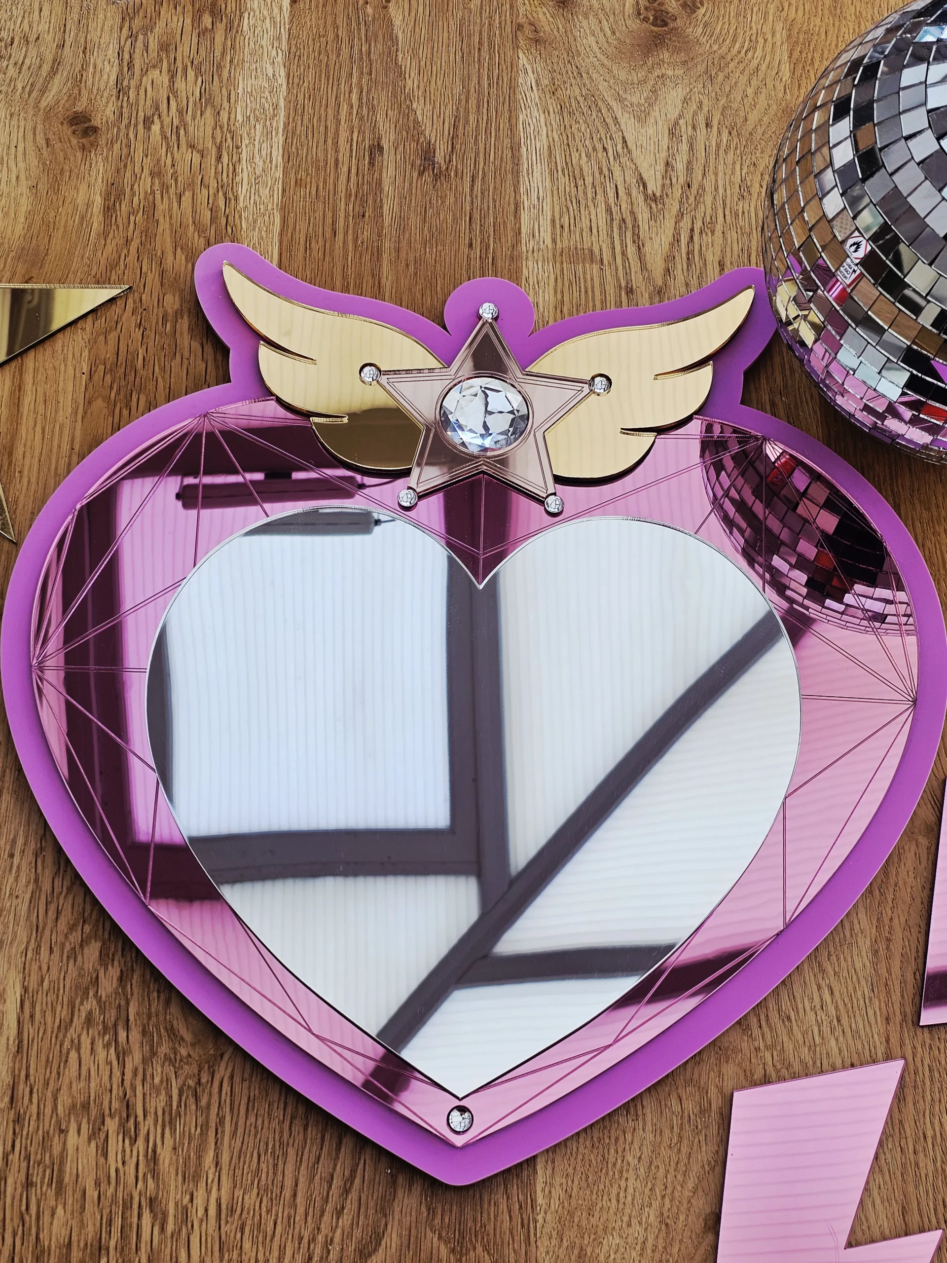 A heart mirror. Woth pink frame, layered with pink and silver heart, with details including gold wings inlaid with crystals.