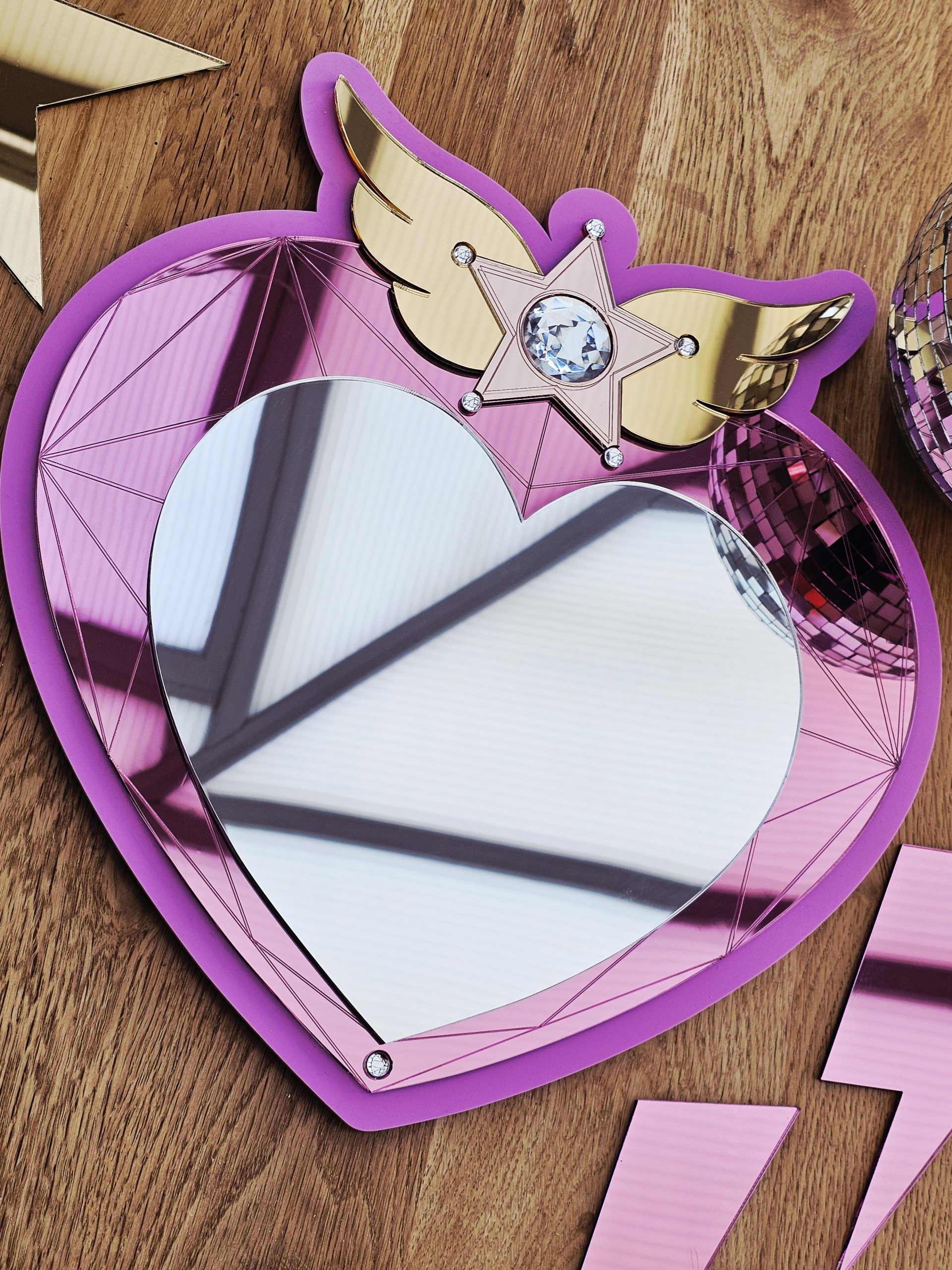 A heart mirror. Woth pink frame, layered with pink and silver heart, with details including gold wings inlaid with crystals.