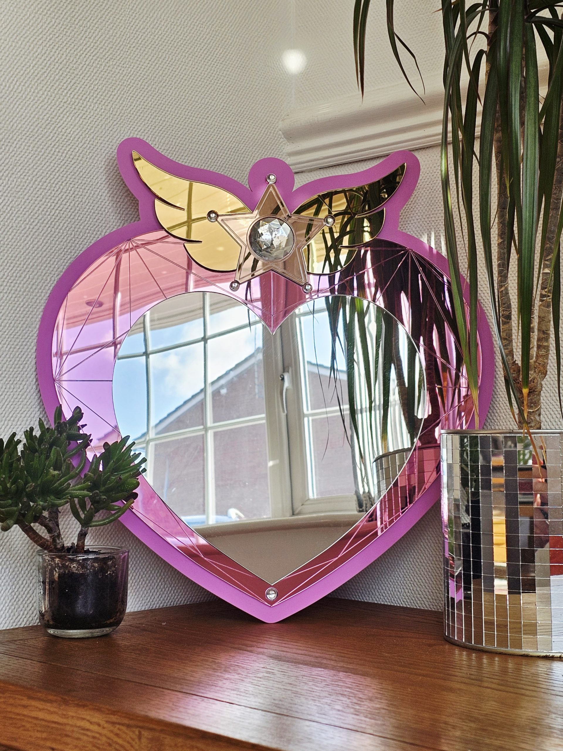 A heart mirror. Woth pink frame, layered with pink and silver heart, with details including gold wings inlaid with crystals.