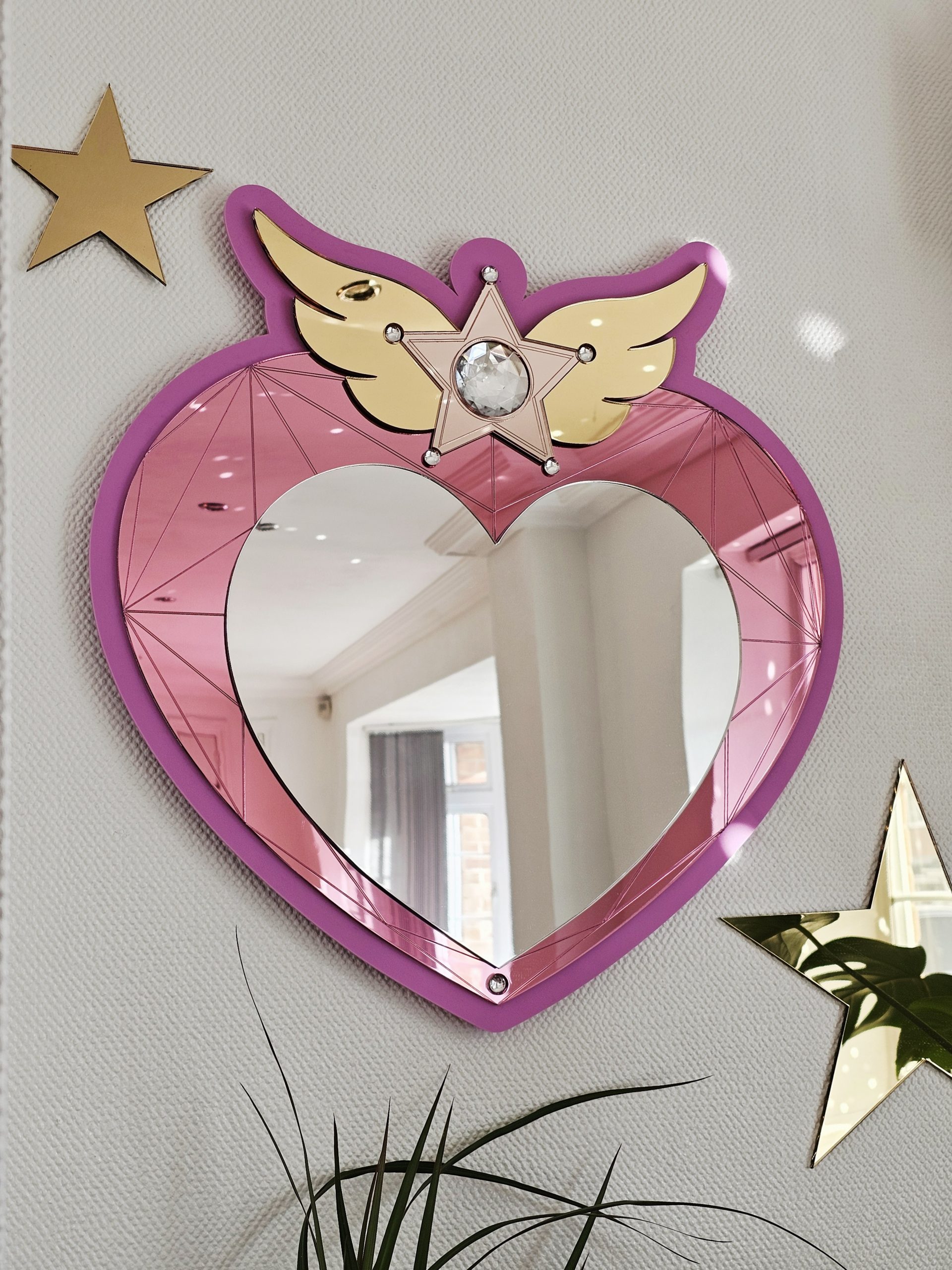 A heart mirror. Woth pink frame, layered with pink and silver heart, with details including gold wings inlaid with crystals.